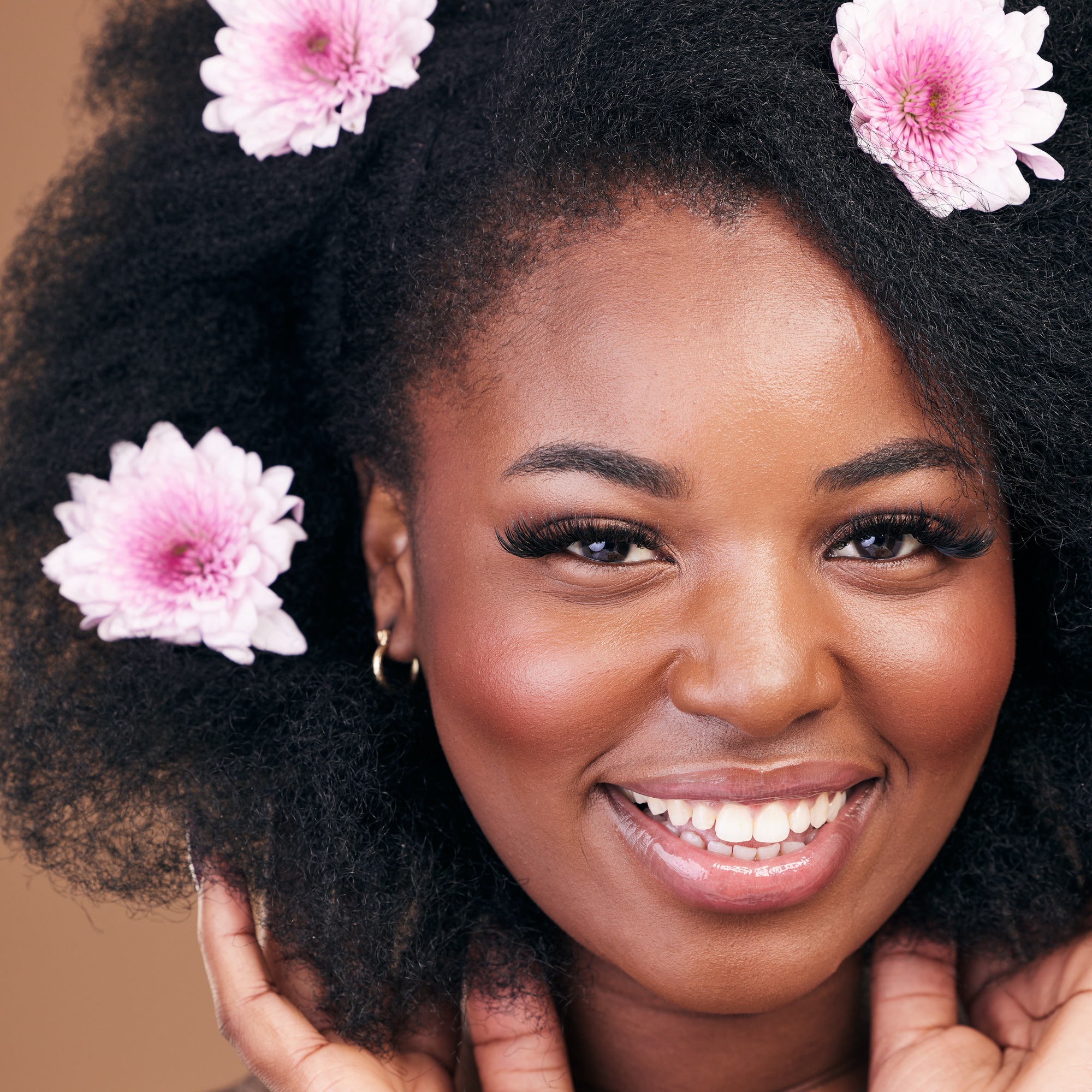 Face, flowers and black woman in afro hair care, happy and beauty in studio isolated on a brown bac